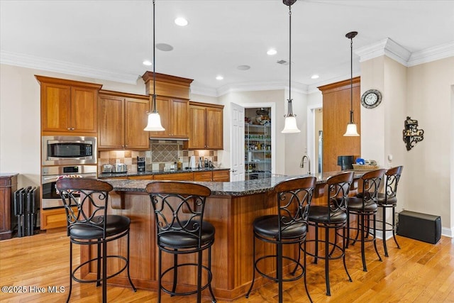 kitchen featuring appliances with stainless steel finishes, decorative light fixtures, a kitchen bar, decorative backsplash, and dark stone counters