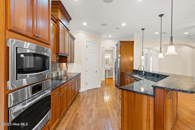 kitchen with hanging light fixtures, dark stone countertops, appliances with stainless steel finishes, light hardwood / wood-style floors, and backsplash