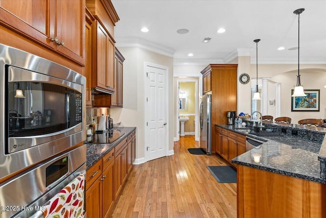 kitchen with appliances with stainless steel finishes, light wood-type flooring, hanging light fixtures, and dark stone counters