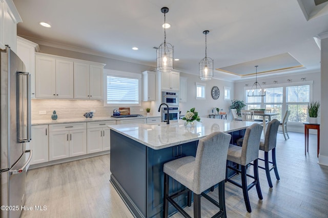 kitchen featuring white cabinetry, stainless steel appliances, pendant lighting, a tray ceiling, and a center island with sink