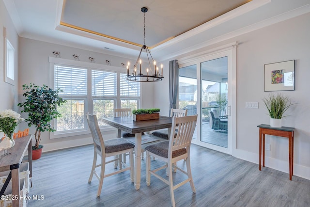 dining area with hardwood / wood-style floors, a notable chandelier, a raised ceiling, and ornamental molding