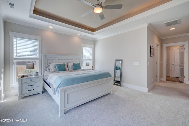 carpeted bedroom featuring ceiling fan, multiple windows, and a tray ceiling