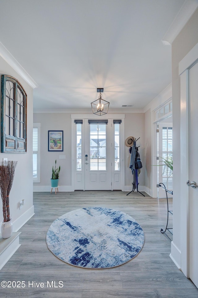 foyer featuring wood-type flooring, ornamental molding, and a notable chandelier