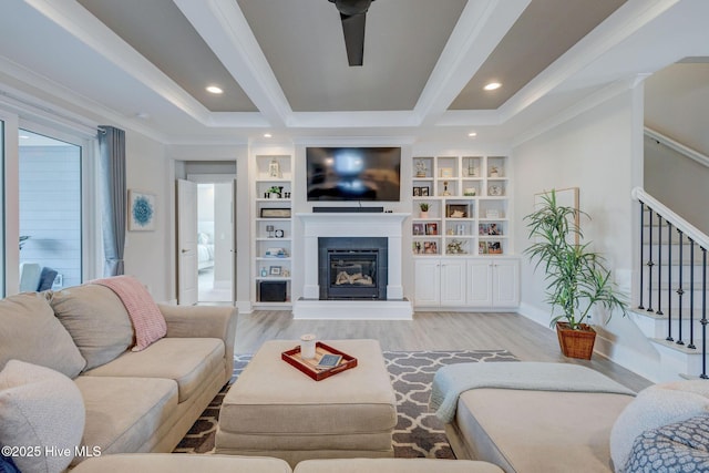 living room featuring built in shelves, ceiling fan, light wood-type flooring, and crown molding