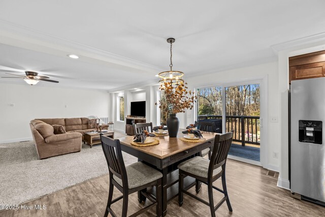 dining space with crown molding, plenty of natural light, ceiling fan with notable chandelier, and hardwood / wood-style flooring