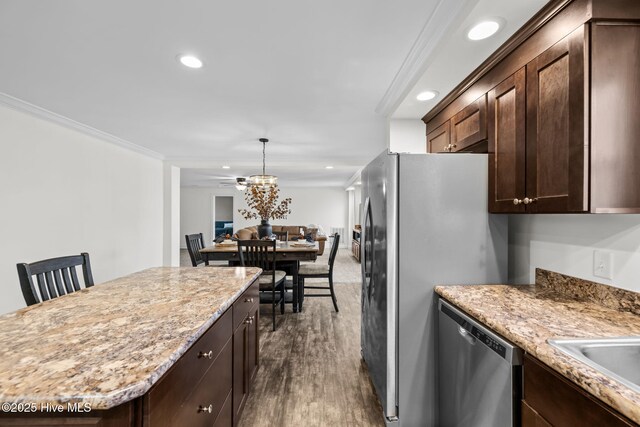 kitchen with hanging light fixtures, dark hardwood / wood-style floors, dark brown cabinets, appliances with stainless steel finishes, and ornamental molding