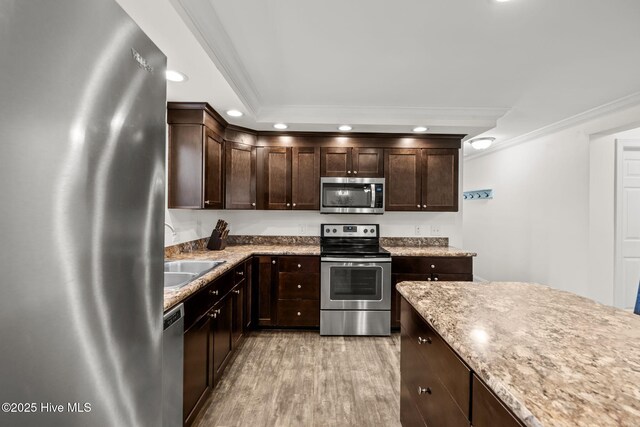 kitchen with appliances with stainless steel finishes, light hardwood / wood-style flooring, dark brown cabinets, and crown molding