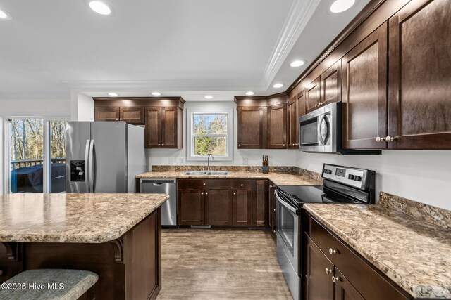 kitchen featuring sink, hardwood / wood-style floors, a breakfast bar, appliances with stainless steel finishes, and ornamental molding