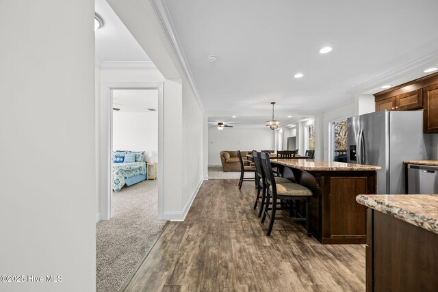 kitchen with dark colored carpet, decorative light fixtures, light stone counters, a breakfast bar area, and stainless steel appliances