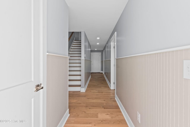 hall with a wainscoted wall, recessed lighting, light wood-type flooring, and stairs