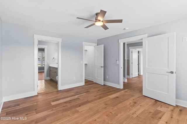 unfurnished bedroom with a walk in closet, ensuite bath, baseboards, and light wood finished floors