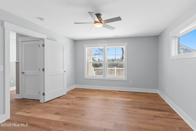 empty room featuring a wealth of natural light, baseboards, ceiling fan, and light wood finished floors