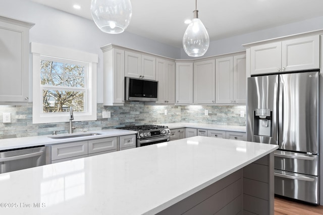 kitchen with a sink, stainless steel appliances, light countertops, decorative light fixtures, and tasteful backsplash