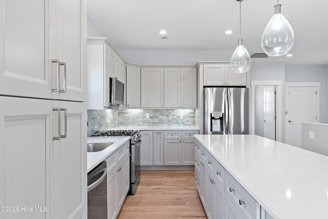 kitchen with decorative backsplash, recessed lighting, light wood-style floors, hanging light fixtures, and stainless steel appliances