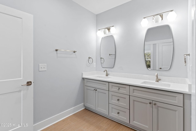 full bathroom featuring a sink, baseboards, wood finished floors, and double vanity