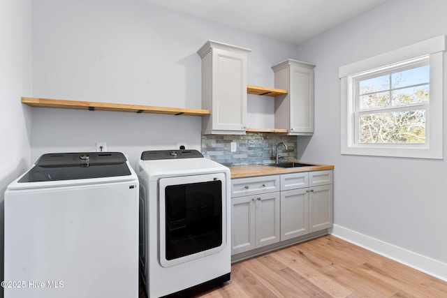 laundry room featuring light wood-type flooring, a sink, cabinet space, baseboards, and washing machine and clothes dryer