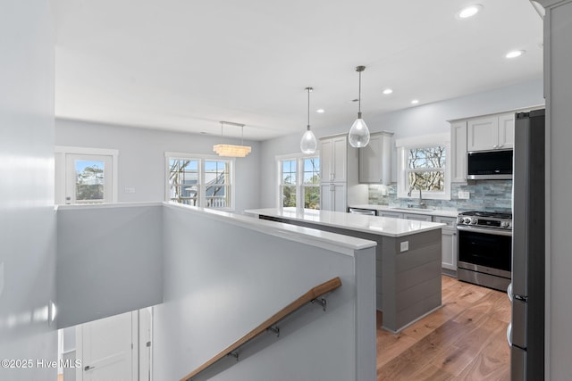 kitchen with a sink, stainless steel appliances, light wood finished floors, decorative backsplash, and light countertops