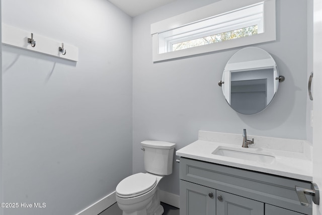 half bath featuring baseboards, toilet, and vanity