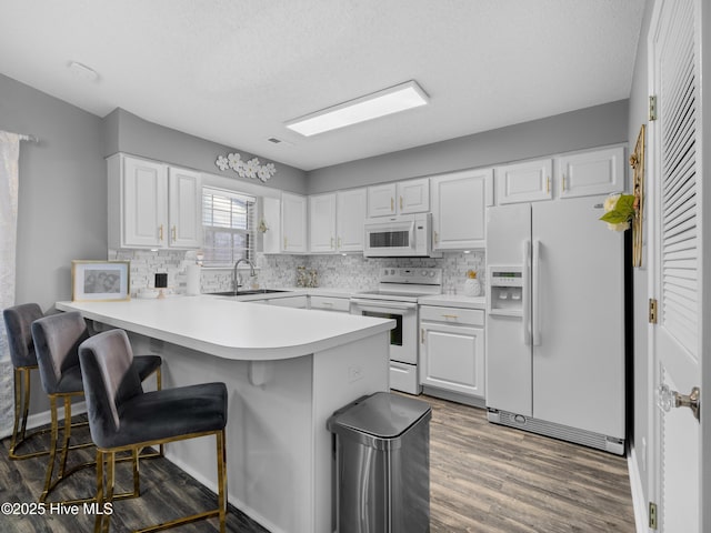 kitchen with white appliances, white cabinets, sink, decorative backsplash, and kitchen peninsula