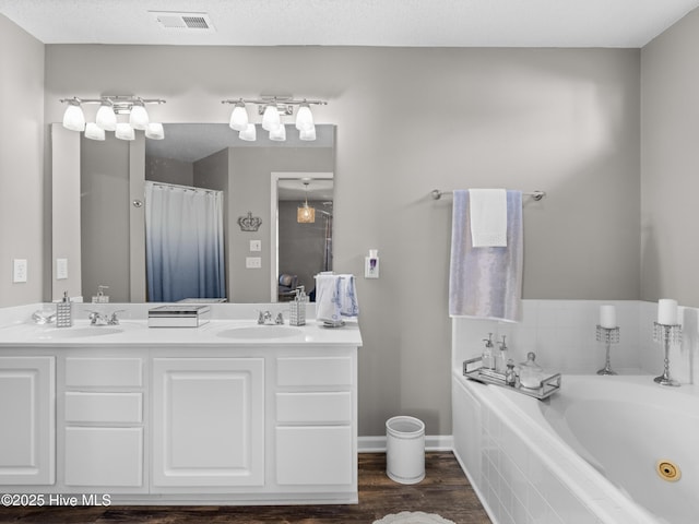 bathroom featuring tiled tub, vanity, wood-type flooring, and a textured ceiling