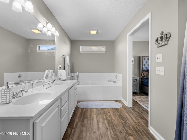 bathroom with vanity, a relaxing tiled tub, wood-type flooring, and a textured ceiling