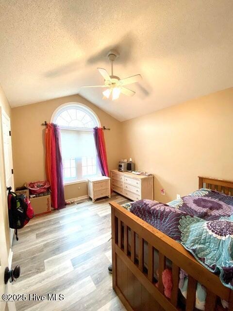 bedroom featuring lofted ceiling, a textured ceiling, ceiling fan, and light hardwood / wood-style flooring