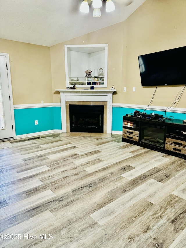 living room with a tile fireplace, lofted ceiling, and light wood-type flooring