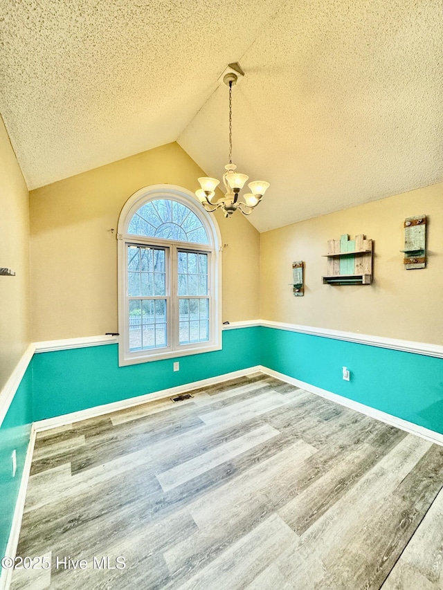 interior space with lofted ceiling, hardwood / wood-style flooring, a chandelier, and a textured ceiling