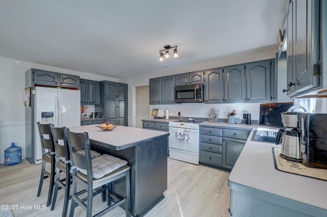 kitchen with a center island, white appliances, backsplash, a kitchen breakfast bar, and light wood-type flooring