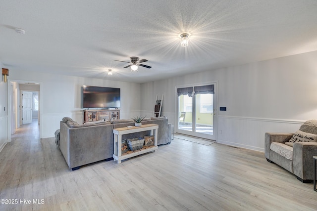 living room featuring ceiling fan, light hardwood / wood-style floors, and a textured ceiling