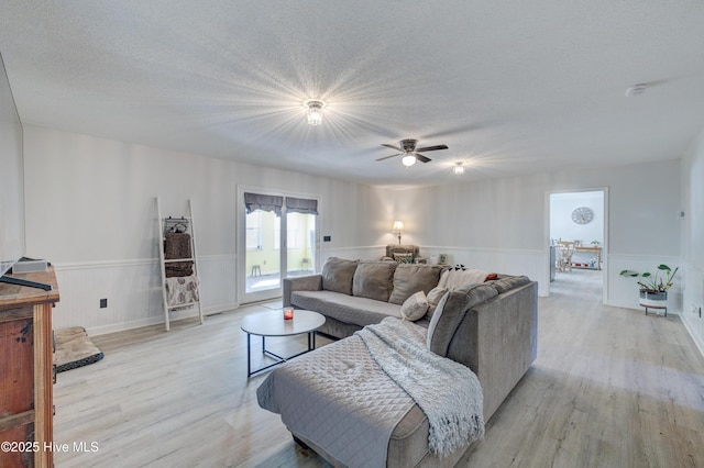 living room featuring ceiling fan, light hardwood / wood-style floors, and a textured ceiling