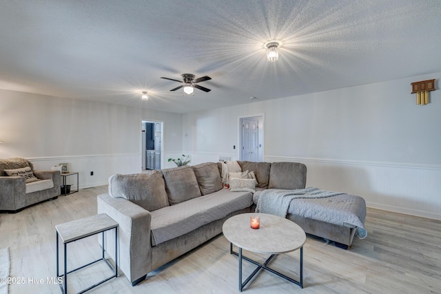 living room with ceiling fan, light wood-type flooring, and a textured ceiling