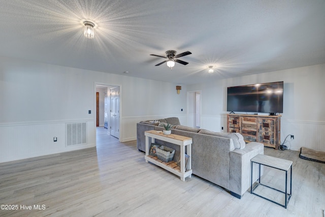 living room featuring ceiling fan, light wood-type flooring, and a textured ceiling