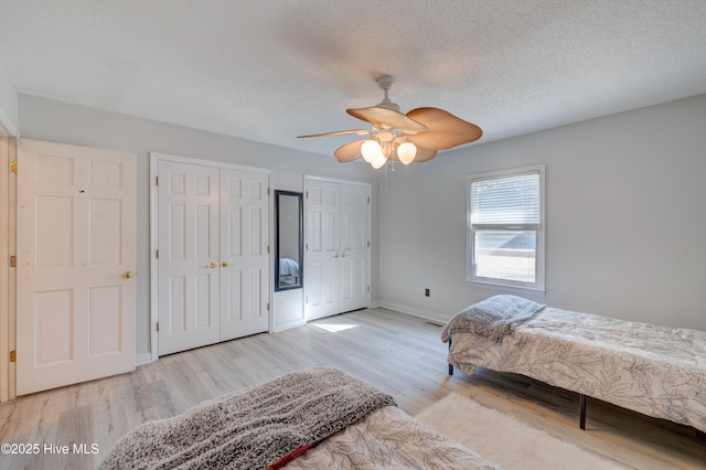 unfurnished bedroom with two closets, ceiling fan, a textured ceiling, and light wood-type flooring