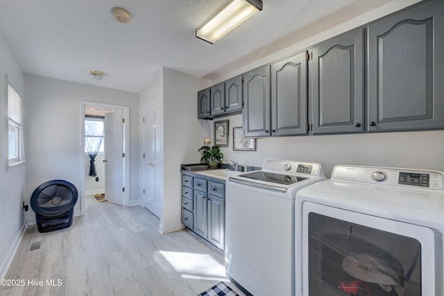 laundry area featuring washer and clothes dryer, cabinets, sink, light hardwood / wood-style flooring, and a textured ceiling