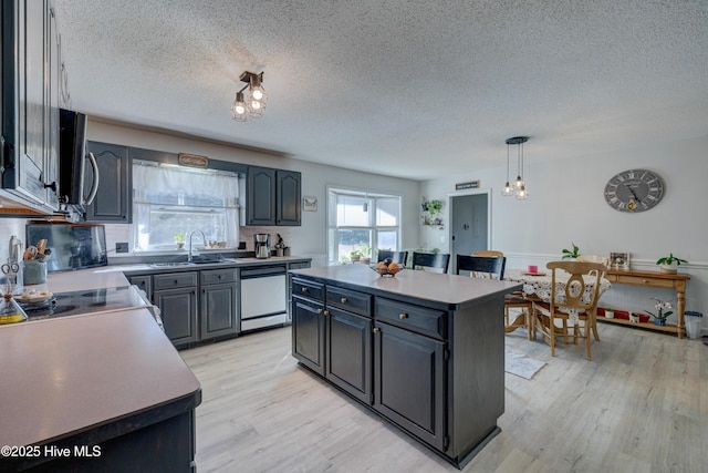 kitchen with a center island, white dishwasher, sink, hanging light fixtures, and light hardwood / wood-style flooring