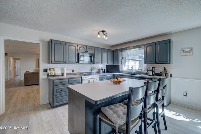 kitchen featuring stainless steel appliances, a kitchen breakfast bar, a textured ceiling, decorative backsplash, and light wood-type flooring