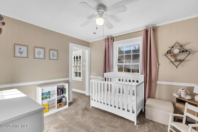 bedroom featuring ornamental molding, a nursery area, light colored carpet, and ceiling fan