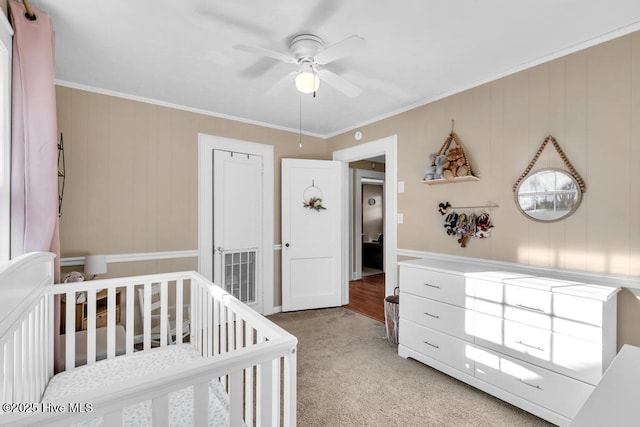 bedroom with a crib, ornamental molding, light carpet, and ceiling fan