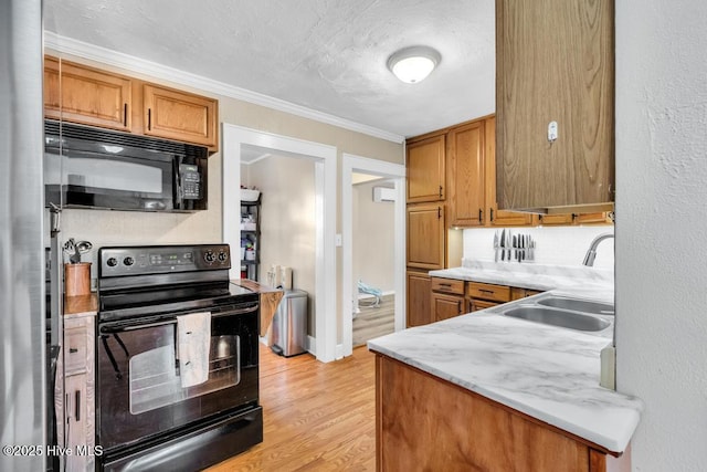 kitchen featuring sink, ornamental molding, light stone counters, black appliances, and light wood-type flooring