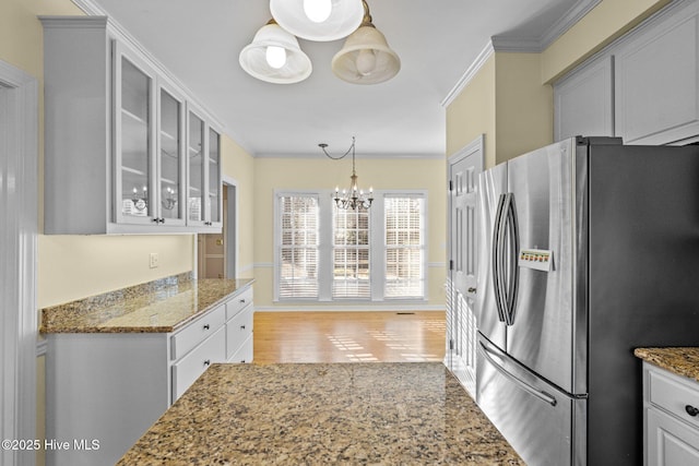 kitchen with crown molding, an inviting chandelier, stone countertops, hanging light fixtures, and stainless steel fridge