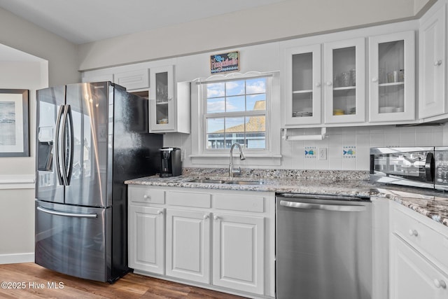 kitchen with hardwood / wood-style floors, white cabinets, sink, light stone countertops, and stainless steel appliances