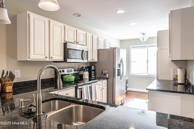 kitchen featuring pendant lighting, stainless steel appliances, white cabinets, dark stone countertops, and sink