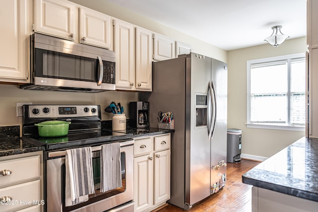 kitchen with appliances with stainless steel finishes, light hardwood / wood-style floors, dark stone countertops, and white cabinetry