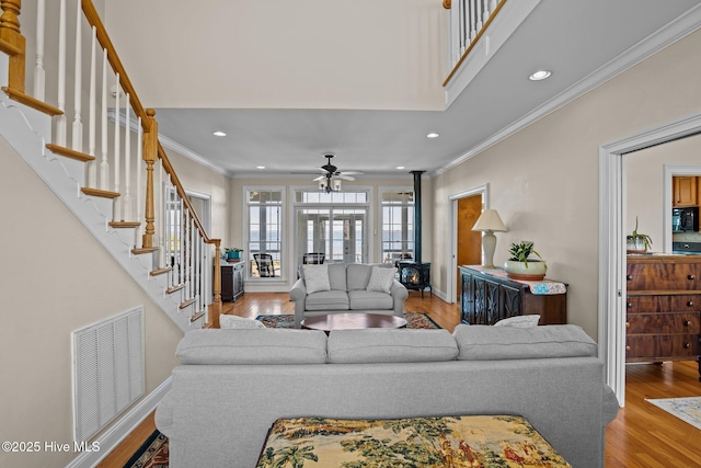 living room featuring crown molding, a wood stove, hardwood / wood-style flooring, ceiling fan, and a high ceiling