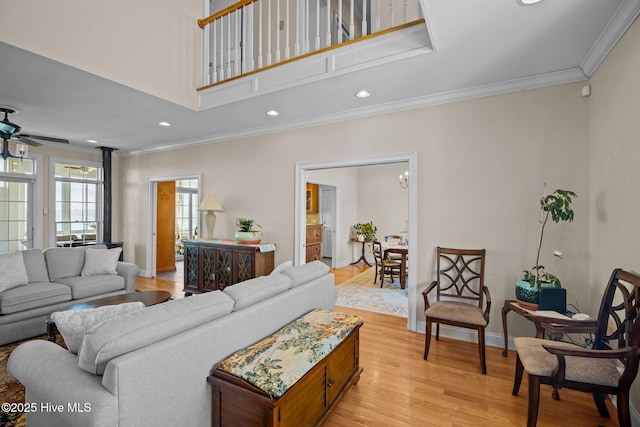 living room featuring a high ceiling, ornamental molding, ceiling fan, and light wood-type flooring