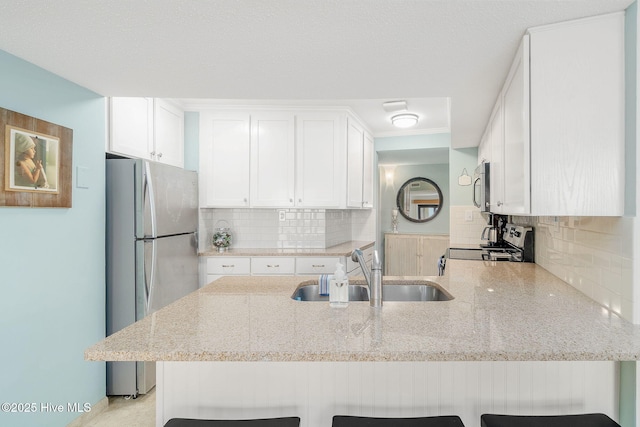 kitchen with kitchen peninsula, appliances with stainless steel finishes, white cabinets, and a kitchen breakfast bar