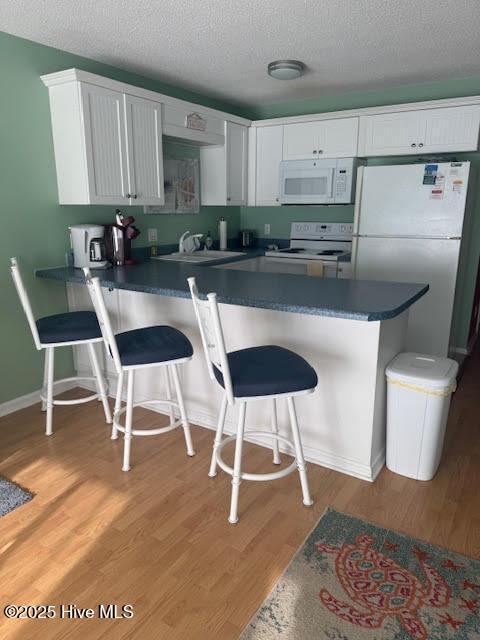 kitchen with white appliances, kitchen peninsula, light hardwood / wood-style flooring, a kitchen bar, and white cabinetry