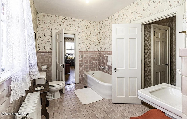 bathroom with toilet, tile patterned flooring, tile walls, a bath, and radiator heating unit