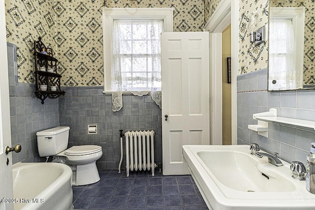 bathroom featuring tile walls, toilet, radiator, and a tub to relax in